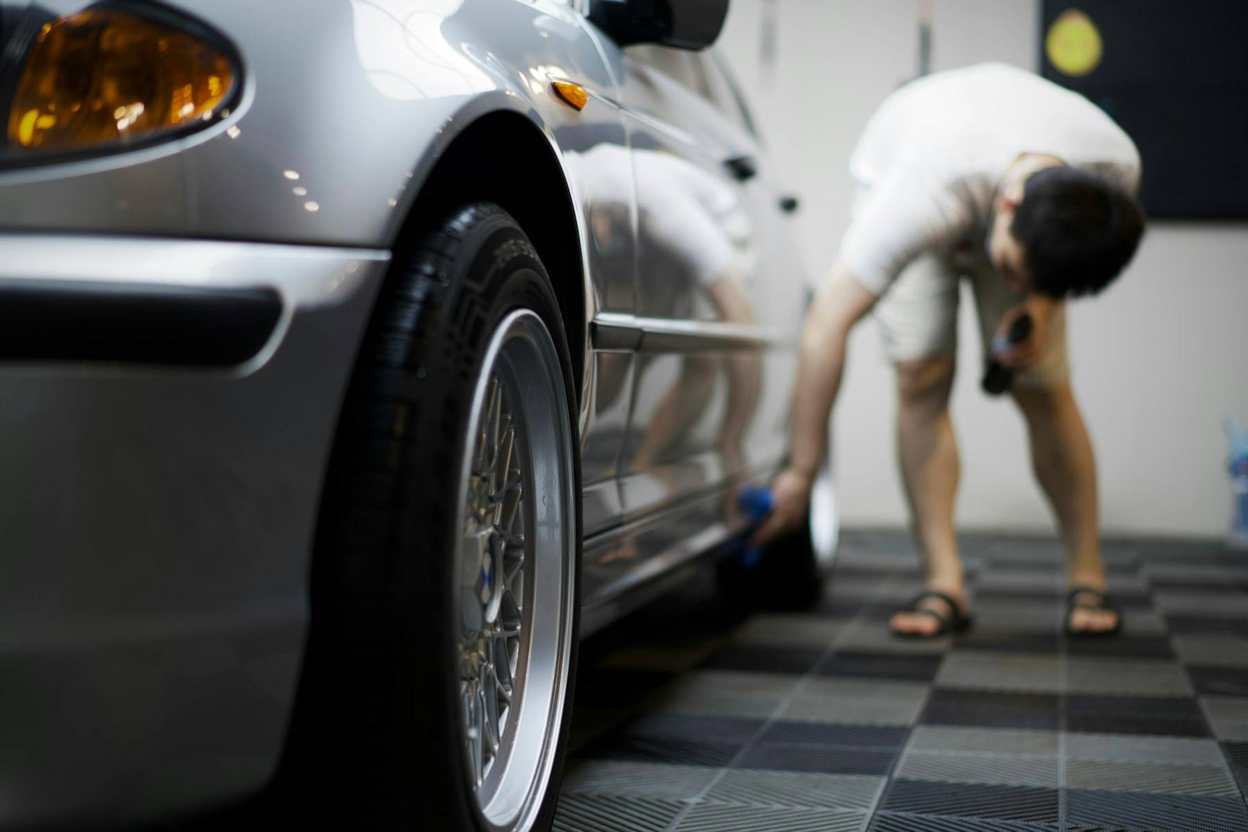 Detailer inspecting a car's lower panel on a checkered studio floor