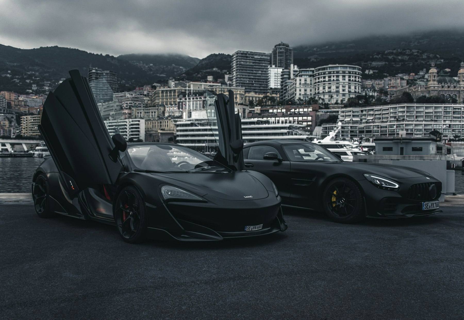 Two matte black sports cars parked on a harbor quay