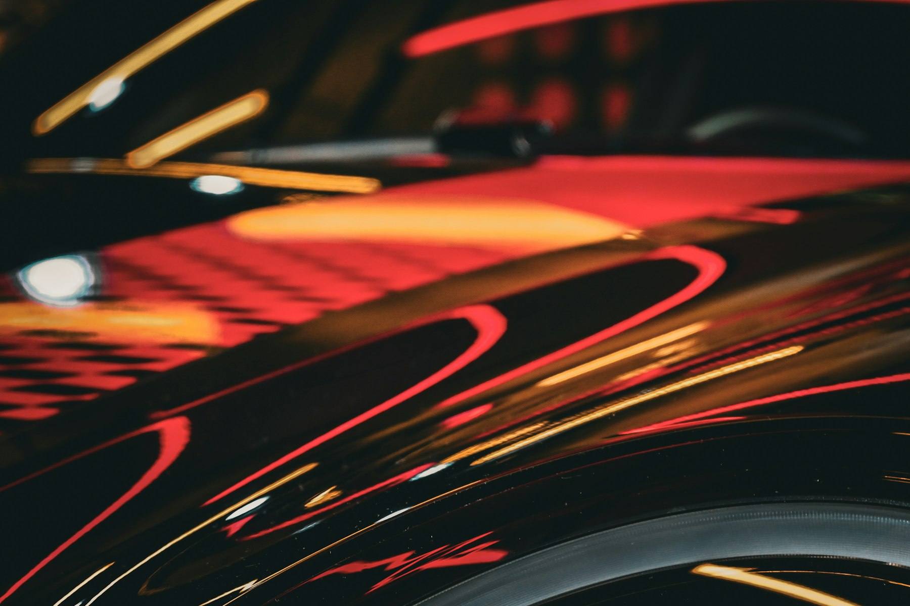 Abstract reflections of warm light across glossy black paint